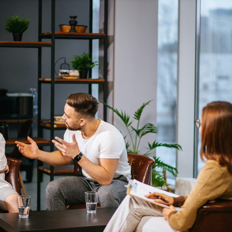 Sesión de Mediación Tres personas en una conversación intensa, con una mujer preocupada y dos personas discutiendo.