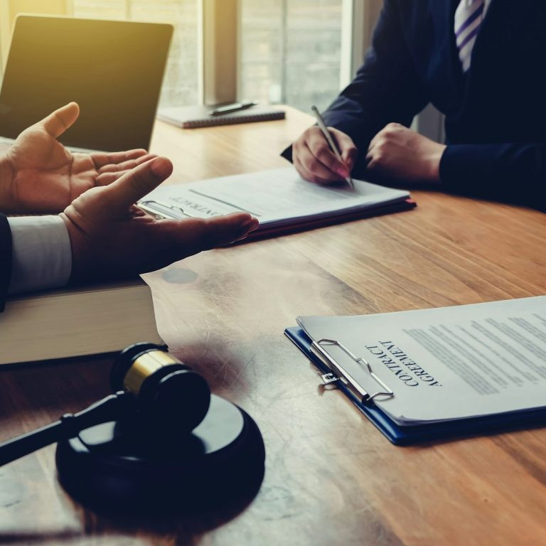 Abogado Dos personas discuten documentos en una mesa, con un mazo de juez en primer plano.