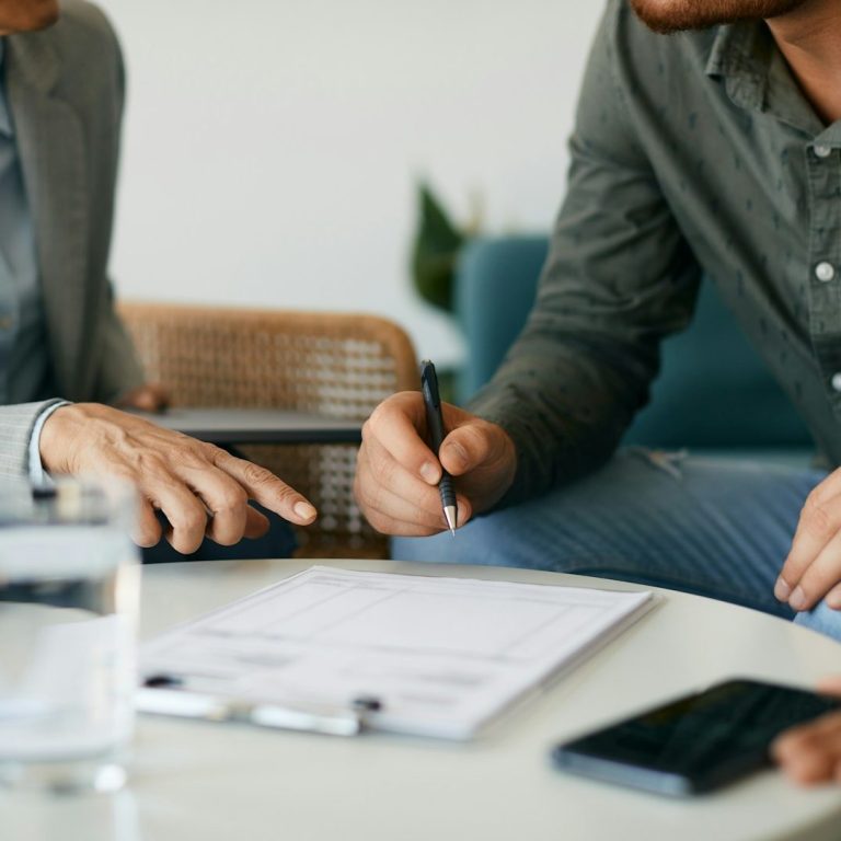 Consulta Gratis Dos personas discuten sobre un documento en una mesa con agua y una calculadora.