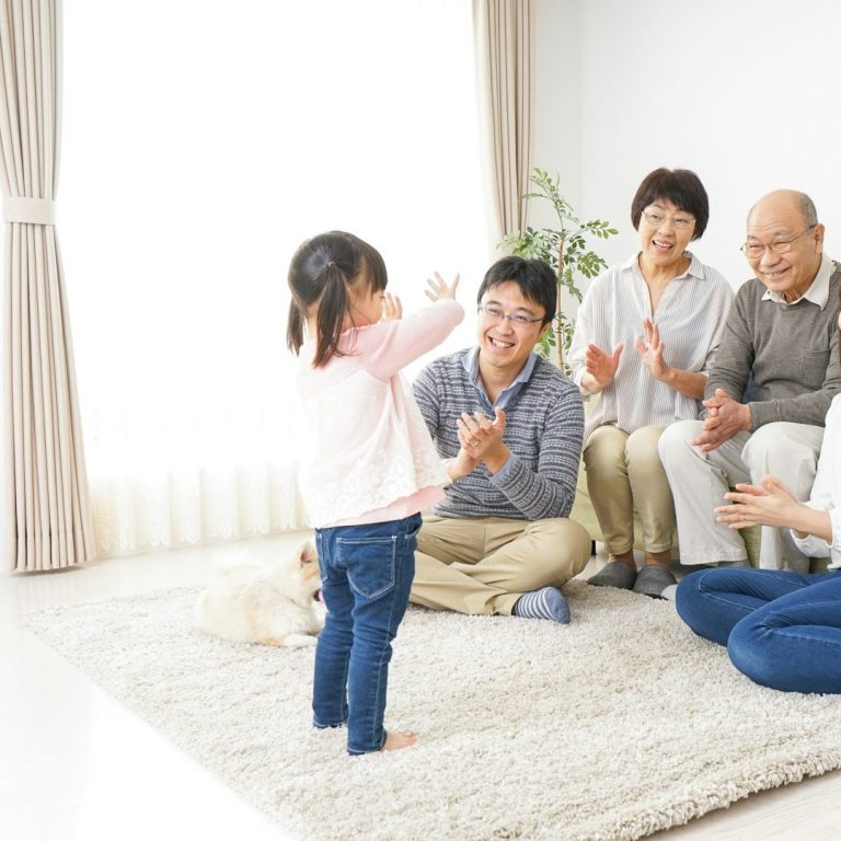 Familia Feliz Niña pequeña aplaudiendo en un salón, rodeada de cuatro adultos sonrientes.